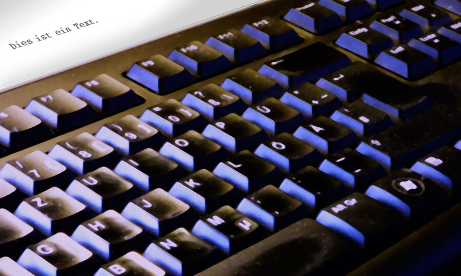 Tastatur mit einem Blatt Papier: „Dies ist ein Text.“